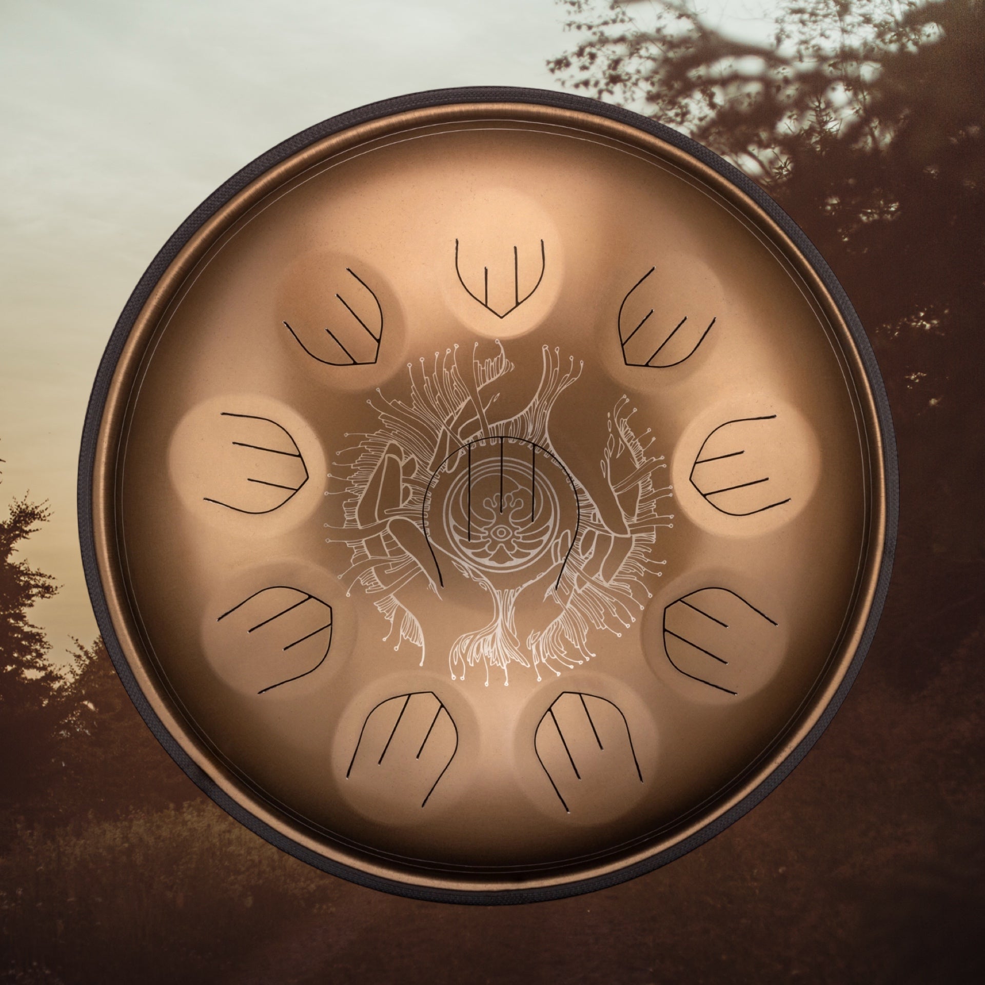 A bronze tongue drum with engraved designs and twelve cut-out tongues, shown against a blurred outdoor background with trees and a cloudy sky. Discover more unique instruments at Yatao Handpan Shop.