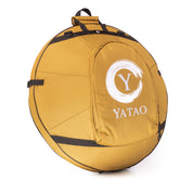 A round, golden-brown padded carrying case with black straps and handle, featuring a large front pocket and white Yatao // Shop logo. Perfect for safely transporting an Ayasa D Kurd 10 handpan or other beginner handpans.