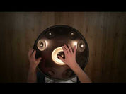 A person plays a YataoPan | D Ashakiran 15 handpan drum, resting it on their lap. The text “YataoPan | D Ashakiran 15” appears on the left. Discover more at a Handpan Shop Germany or Buy Handpan online.